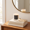 Double-wick Magnetic Reserve candle burning on a stack of books beside wick trimmers, reflected in a round mirror