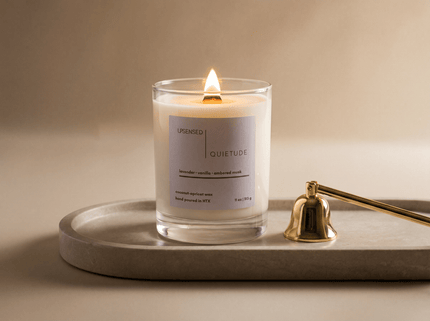 Luxury Upsensed candle with a wooden wick burning on a stone tray beside a gold candle snuffer — illustrating what sets luxury candles apart from regular candles.