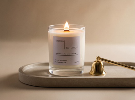 Luxury Upsensed candle with a wooden wick burning on a stone tray beside a gold candle snuffer — illustrating what sets luxury candles apart from regular candles.