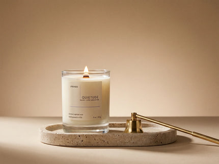 Premium Upsensed candle with a wooden wick burning on a stone tray beside a gold candle snuffer.