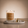 Double-wick Leather + Tabac candle on a stone tray beside a brass candle snuffer