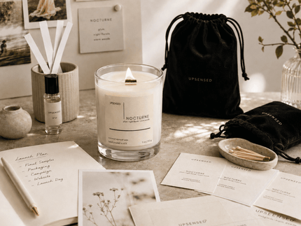 Upsensed Nocturne candle with black velvet drawstring bags, fragrance blotters, launch planning notes, and scent development materials in a warm editorial workspace.