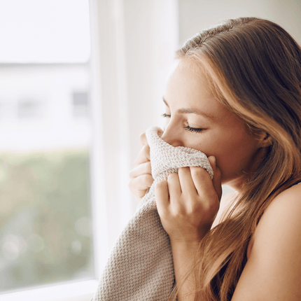 Woman inhaling scent from a towel by a sunlit window, representing the psychology of scent and emotional memory