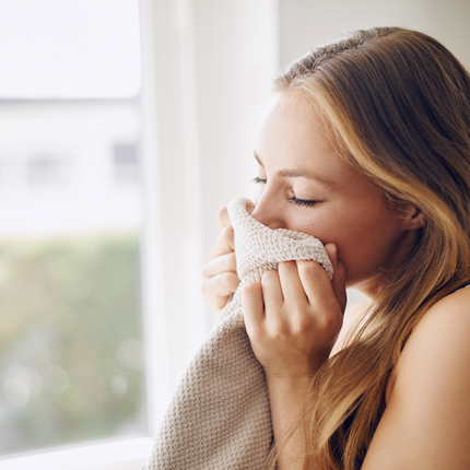 Woman inhaling scent from a towel by a sunlit window, representing the psychology of scent and emotional memory