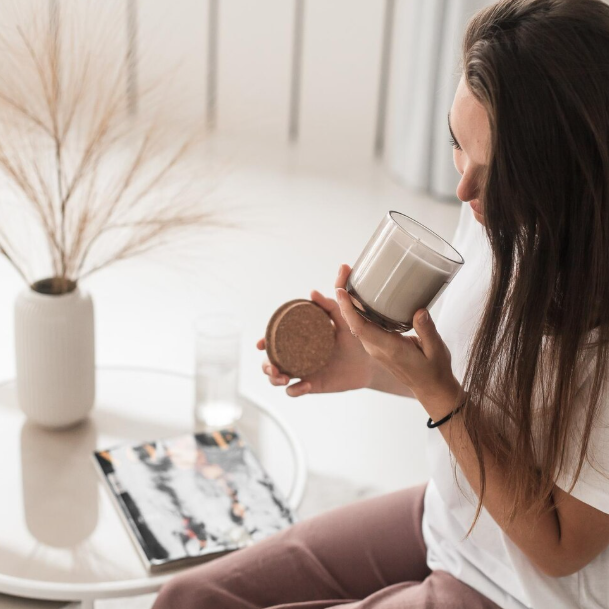 Woman smelling a candle with a plant and magazine in the background