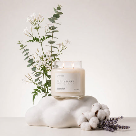 Upsensed Cloudwash candle burning atop a cloud-shaped sculpture, styled with jasmine and eucalyptus branches, cotton bolls, and lavender sprigs.
