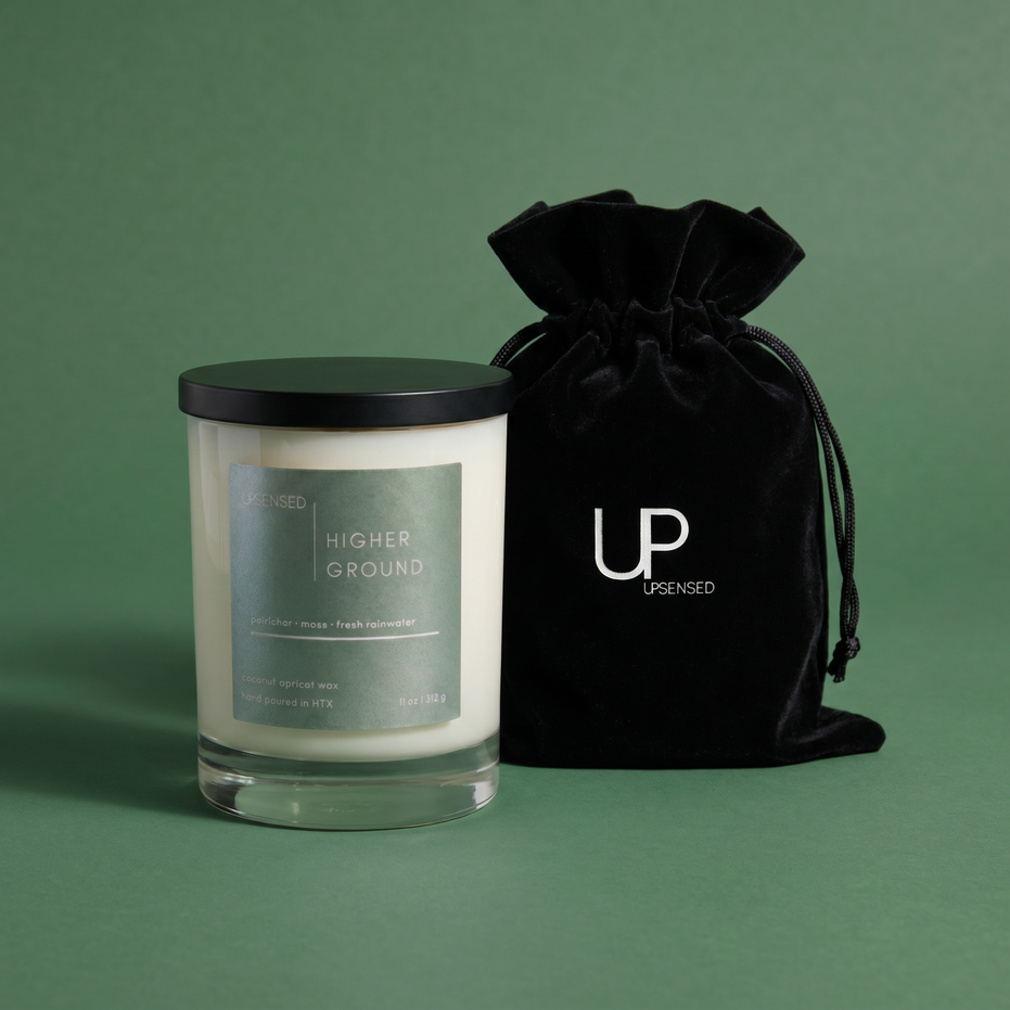 Upsensed Higher Ground 11oz scented candle with black velvet drawstring gift bag on sage green background - petrichor moss and rainwater coconut apricot wax candle hand poured in Houston