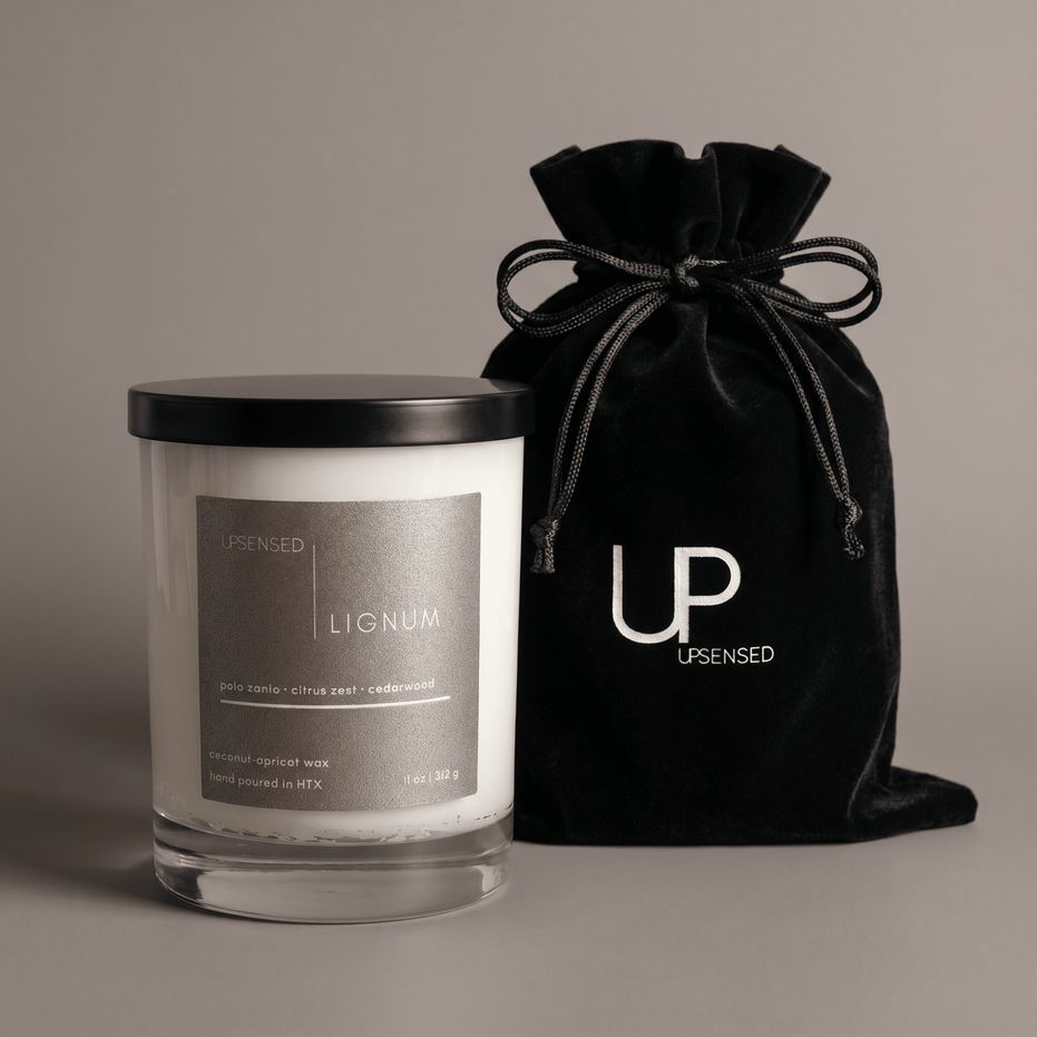 Lignum candle in a clear glass jar with a black lid beside a black Upsensed velvet drawstring bag.