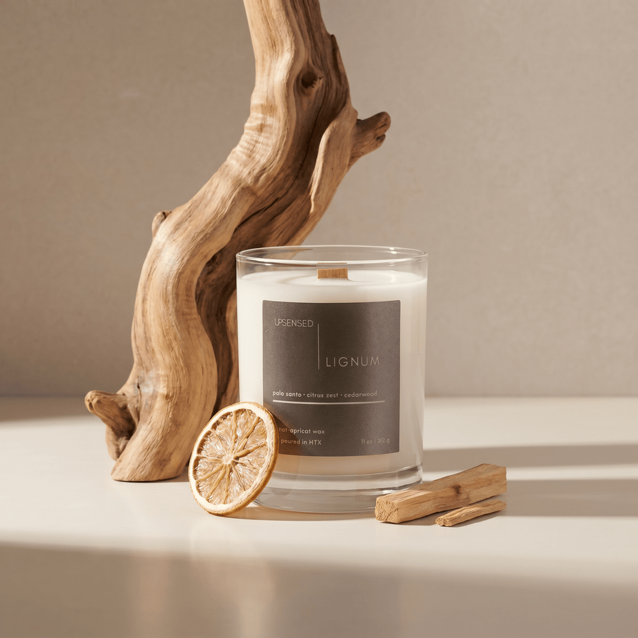 Lignum candle styled with palo santo wood, dried citrus, and natural wood accents on a warm neutral surface.