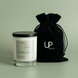 Moss candle in a clear glass jar with a black lid beside a black Upsensed velvet drawstring bag on a soft green background.