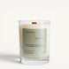 Lit Moss candle in a clear glass jar with a pale green label and wooden wick on a clean white background.