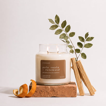 Upsensed Palo Santo + Rosewood candle burning on a terracotta brick, styled with a leafy branch, palo santo sticks, and a curled orange peel.