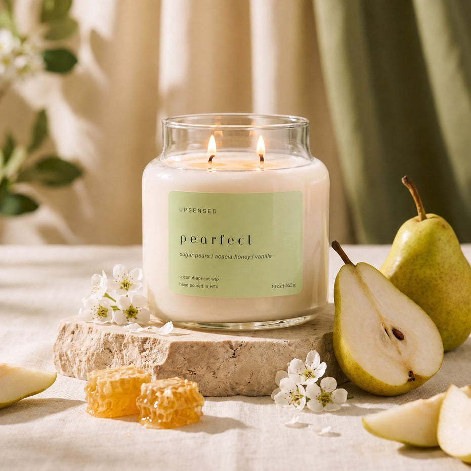 Upsensed Pearfect candle on a stone slab in front of draped curtains, styled with pear blossoms, honeycomb pieces, and fresh pear halves and slices.