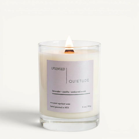 Lit Quietude candle in a clear glass jar with a lavender label and wooden wick on a clean white background.