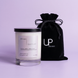 Quietude candle in a clear glass jar with a black lid beside a black Upsensed velvet drawstring bag on a soft lavender background.