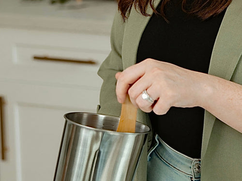Upsensed founder hand stirring candle wax in a metal pouring pitcher during the small-batch candle making process.