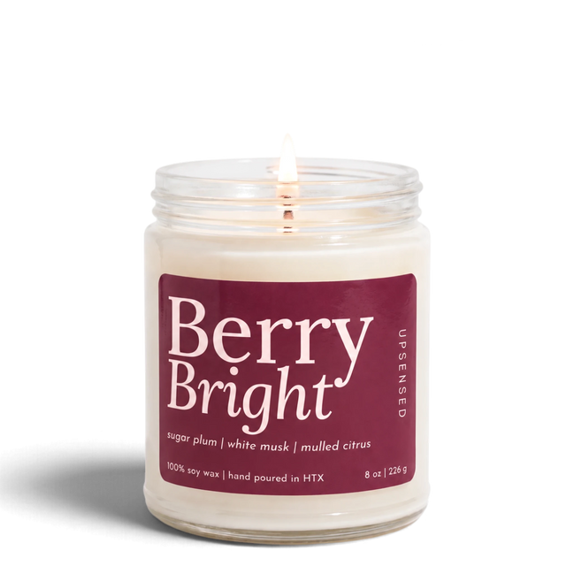 Upsensed Berry Bright 8 oz soy candle, lit, in a clear glass jar with a deep berry label listing sugar plum, white musk, and mulled citrus
