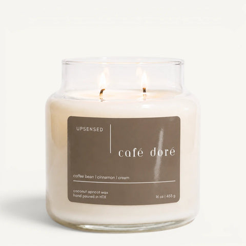 Upsensed Café Doré 16 oz double-wick candle in a clear apothecary jar with a brown label, coffee bean, cinnamon, and cream scent notes, on a plain white background.