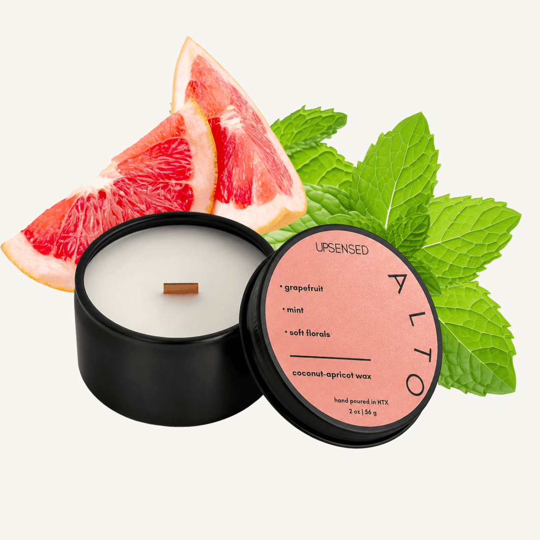  Upsensed Alto 2 oz mini candle in a matte black tin with warm peach lid, surrounded by fresh grapefruit wedges and vibrant green mint leaves