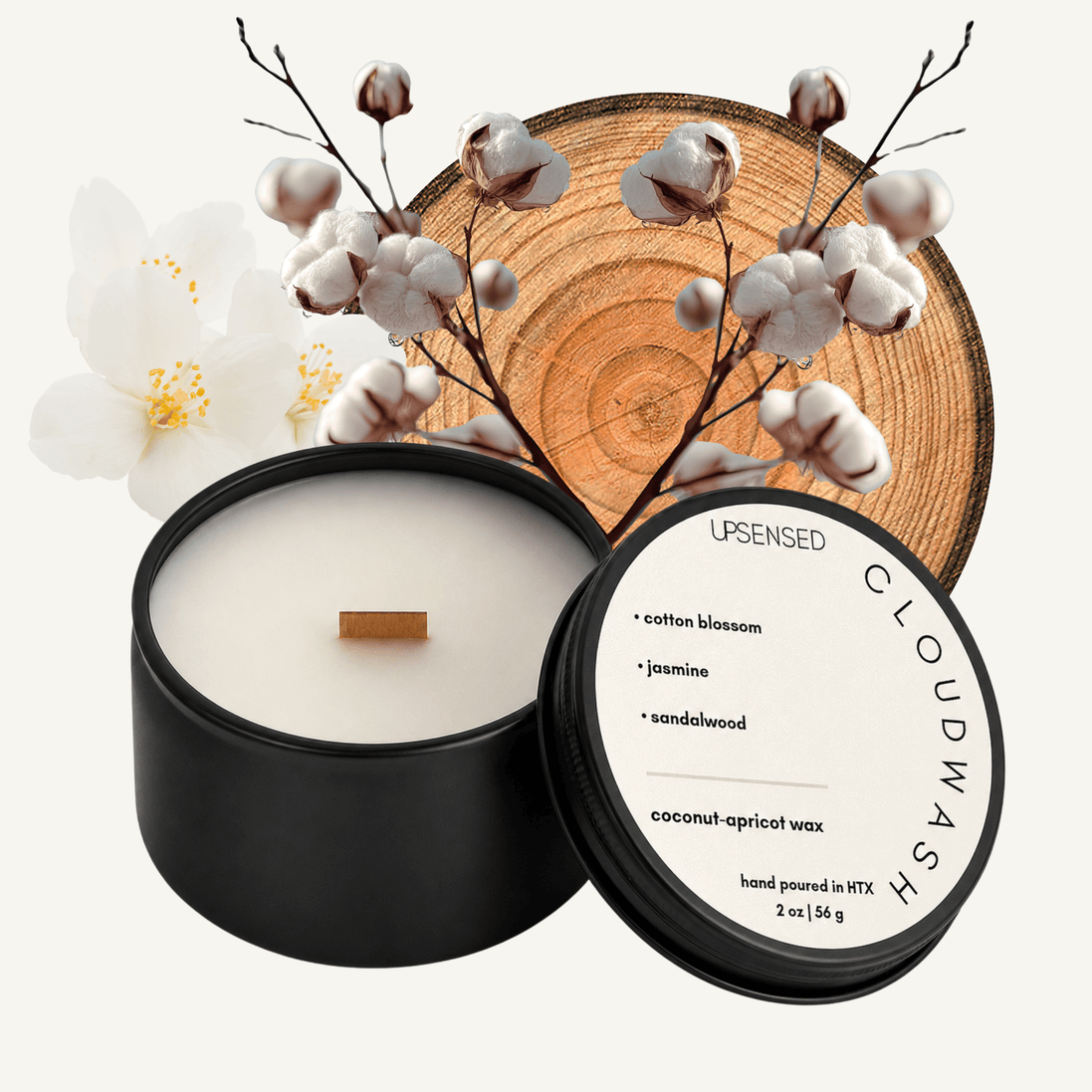 Upsensed Cloudwash 2 oz mini candle in a matte black tin with soft white lid, surrounded by cotton branches, a white jasmine bloom, and a natural wood slice