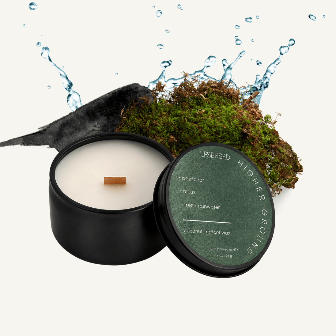 Upsensed Higher Ground 2 oz mini candle in a matte black tin with deep forest green lid, surrounded by a moss-covered rock and a dramatic water splash