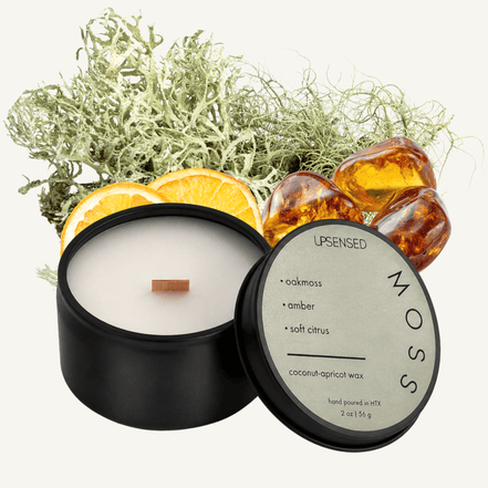 Upsensed Moss 2 oz mini candle in a matte black tin with sage green lid, surrounded by dried moss, amber resin stones, and orange slices