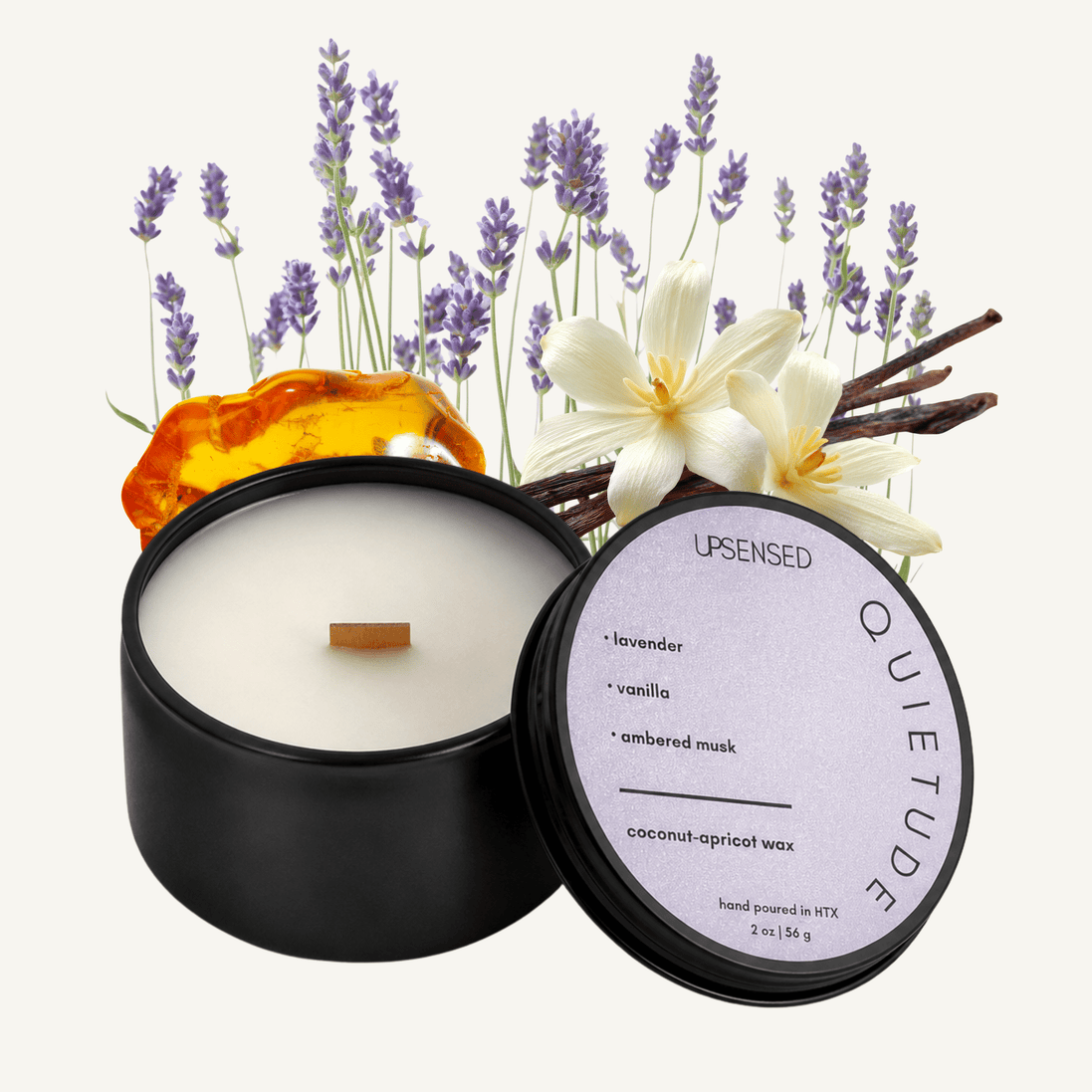Upsensed Quietude 2 oz mini candle in a matte black tin with soft lavender lid, surrounded by purple lavender stems, a white vanilla orchid, and amber resin