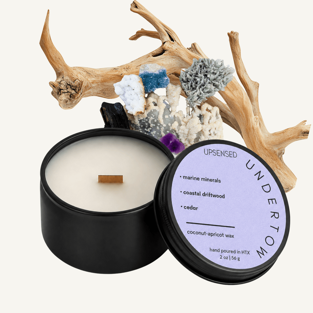 Upsensed Undertow 2 oz mini candle in a matte black tin with soft lilac lid, surrounded by driftwood branches and colorful mineral crystals