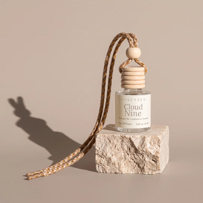 Cloud Nine car diffuser on a cream travertine block against a warm greige backdrop