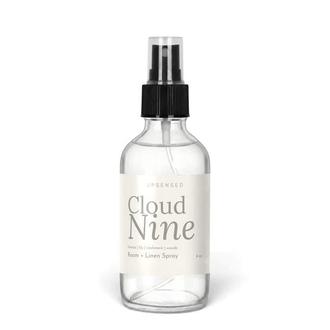 Cloud Nine 4 oz room and linen spray by Upsensed in a clear glass bottle with a black sprayer and a soft cream label in warm gray type listing freesia, lily, cashmere, and woods notes.