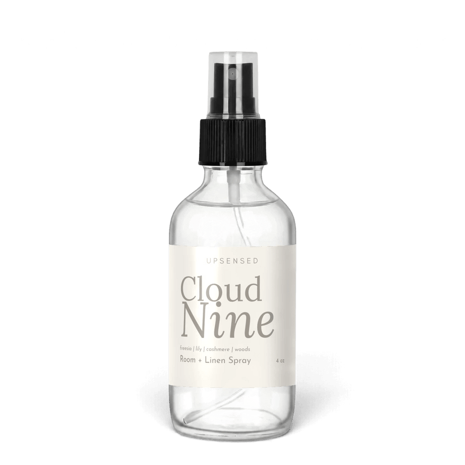 Cloud Nine 4 oz room and linen spray by Upsensed in a clear glass bottle with a black sprayer and a soft cream label in warm gray type listing freesia, lily, cashmere, and woods notes.