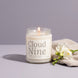 Lit Cloud Nine 8 oz soy candle in a clear glass jar beside white freesia and a cream knit throw on a soft lavender backdrop