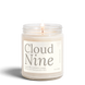 Cloud Nine 8 oz soy candle by Upsensed, lit, in a clear glass jar with a soft cream label in warm gray type listing freesia, lily, cashmere, and woods notes.