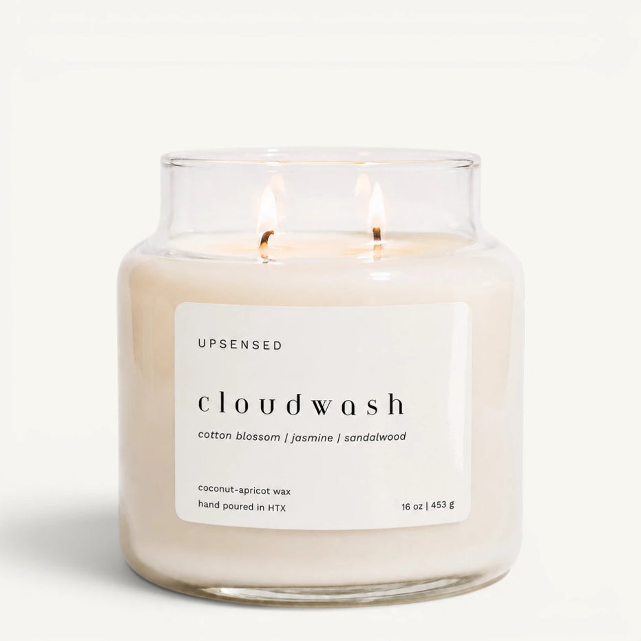 Upsensed Cloudwash 16 oz double-wick candle in a clear apothecary jar with a white label, cotton blossom, jasmine, and sandalwood scent notes, on a plain white background.