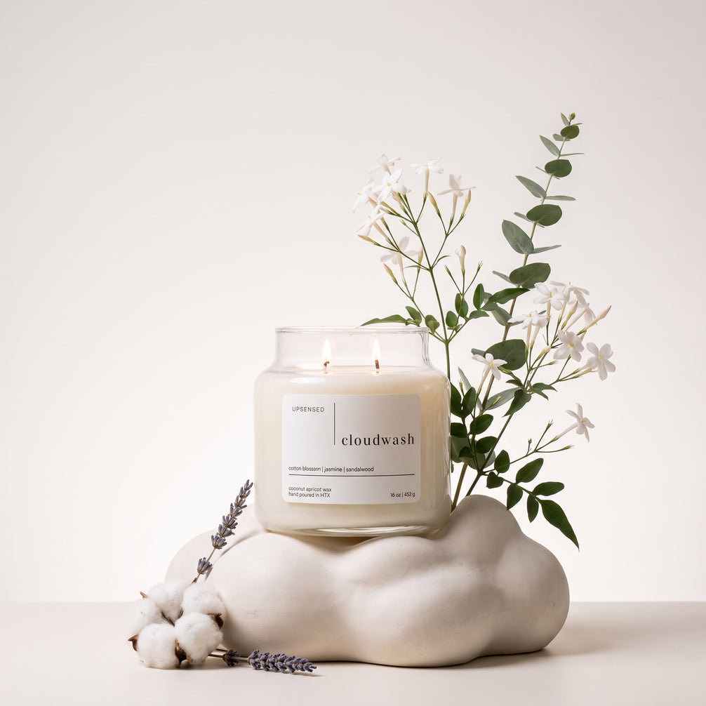Upsensed Cloudwash candle burning atop a cloud-shaped ceramic sculpture, styled with jasmine and eucalyptus branches, cotton bolls, and sprigs of lavender.