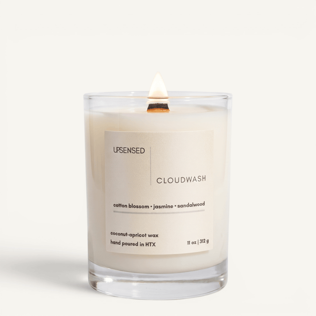 Upsensed Cloudwash candle lit on white background, showing cream label with cotton blossom, jasmine, and sandalwood notes
