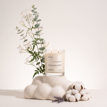 Upsensed Cloudwash candle styled with jasmine blooms, eucalyptus, lavender, and raw cotton on a cloud-shaped pedestal.