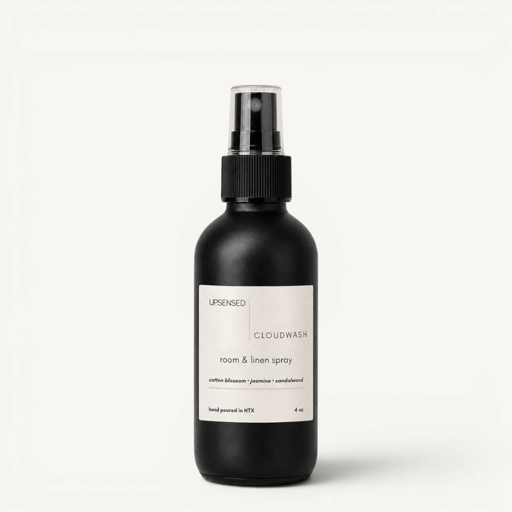 A matte black room & linen spray bottle with a white label, featuring the brand name 'Upsensed' and product name 'Cloudwash', set against a clean off-white background.