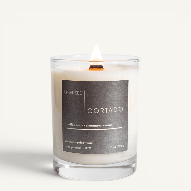 Upsensed Cortado candle lit on white background, showing charcoal label with coffee bean, cinnamon, and cream notes