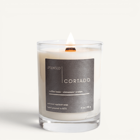 Upsensed Cortado candle lit on white background, showing charcoal label with coffee bean, cinnamon, and cream notes