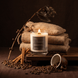 Upsensed Cortado candle burning on a wood platform surrounded by coffee beans, cinnamon sticks, and burlap coffee sacks against a dark moody background
