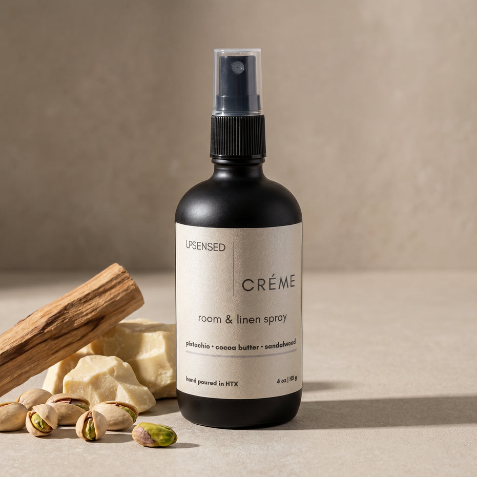 Upsensed Creme Room and Linen Spray beside pistachios raw cocoa butter and sandalwood sticks - warm gourmand home fragrance hand poured in Houston