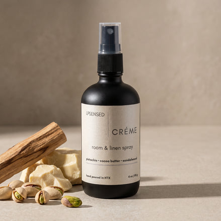 Upsensed Creme Room and Linen Spray beside pistachios raw cocoa butter and sandalwood sticks - warm gourmand home fragrance hand poured in Houston