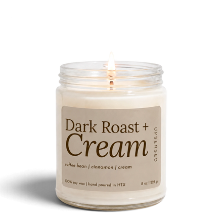 Upsensed Dark Roast + Cream 8 oz soy candle, lit, in a clear glass jar with a latte-toned label and espresso lettering listing coffee bean, cinnamon, and cream