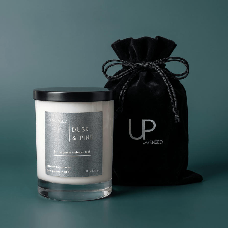 Upsensed Dusk & Pine candle beside reusable black velvet drawstring gift bag on deep teal background