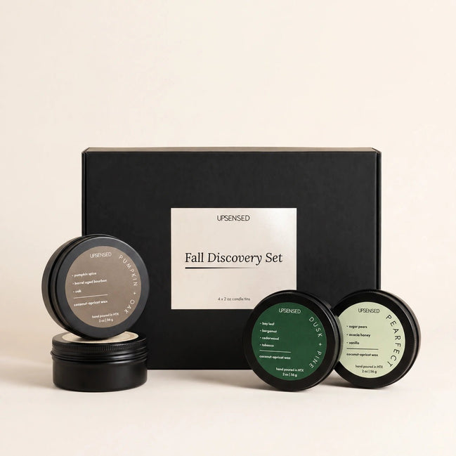 An Upsensed 'Fall Discovery Set' featuring a matte black gift box with a white label, accompanied by four round black cosmetic tins with dark green and off-white labels, arranged on a light beige background.