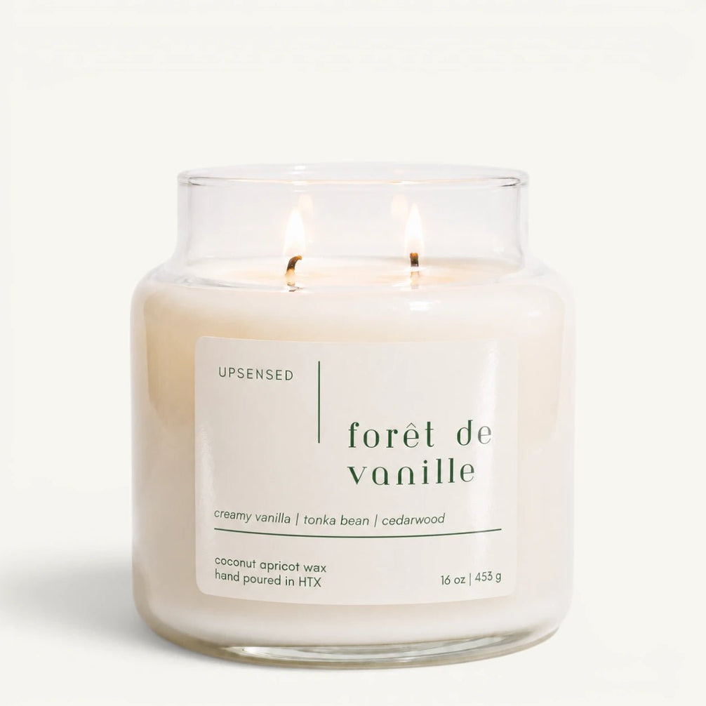 Upsensed Forêt de Vanille 16 oz double-wick candle in a clear apothecary jar with a cream label, creamy vanilla, tonka bean, and cedarwood scent notes, on a plain white background.