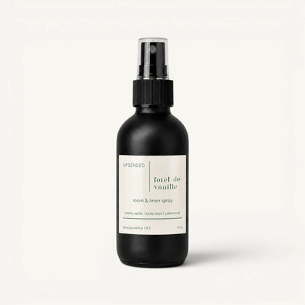 Upsensed Forêt de Vanille room and linen spray in a matte black 4 oz bottle with a cream label, creamy vanilla, tonka bean, and cedarwood scent notes, on a plain white background.