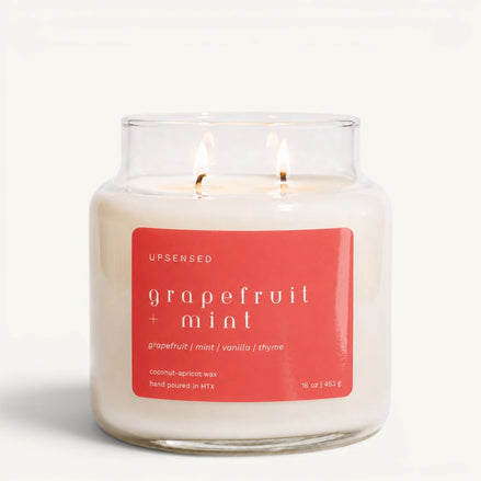 Upsensed Grapefruit + Mint 16 oz double-wick candle in a clear apothecary jar with a coral red label, grapefruit, mint, vanilla, and thyme scent notes, on a plain white background.