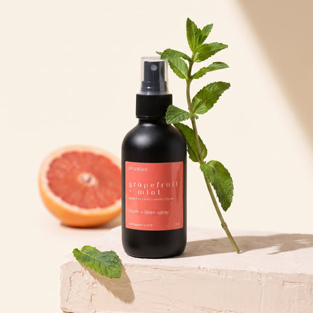 Grapefruit + Mint room and linen spray on a plaster ledge with a mint sprig and halved grapefruit.